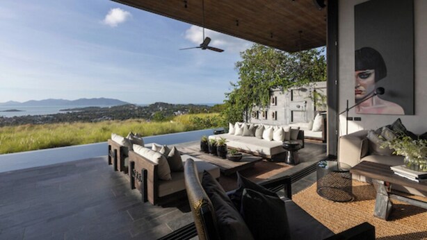 A modern outdoor living space with a view of the sea, a ceiling fan, and a large painting. - Villa Suwan -The Hilltop Escape Samui (Koh Samui)