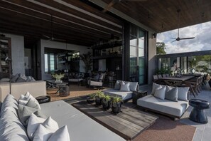 A modern outdoor living area with a sofa, dining table, and chairs, surrounded by potted plants and a wooden deck. - Villa Suwan -The Hilltop Escape Samui (Koh Samui)