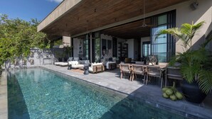 A modern outdoor pool area with a wooden deck, lounge chairs, and a dining setup. - Villa Suwan -The Hilltop Escape Samui (Koh Samui)