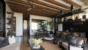 A modern living area with a sofa, coffee table, and chairs, a kitchen in the background, and a ceiling with wooden beams. - Villa Suwan -The Hilltop Escape Samui (Koh Samui)