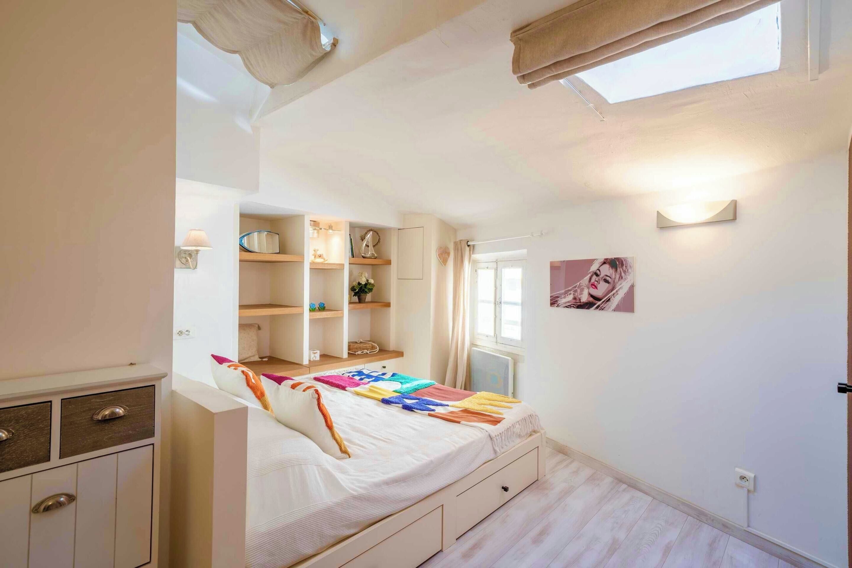 A bedroom with a bed, built-in shelves, a radiator, and a window.