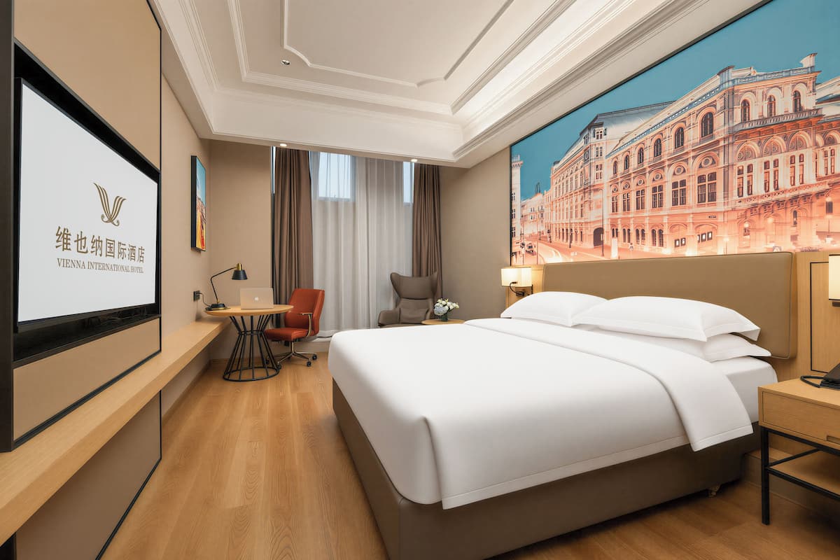 A hotel room with a bed, desk, chair, and a large window.