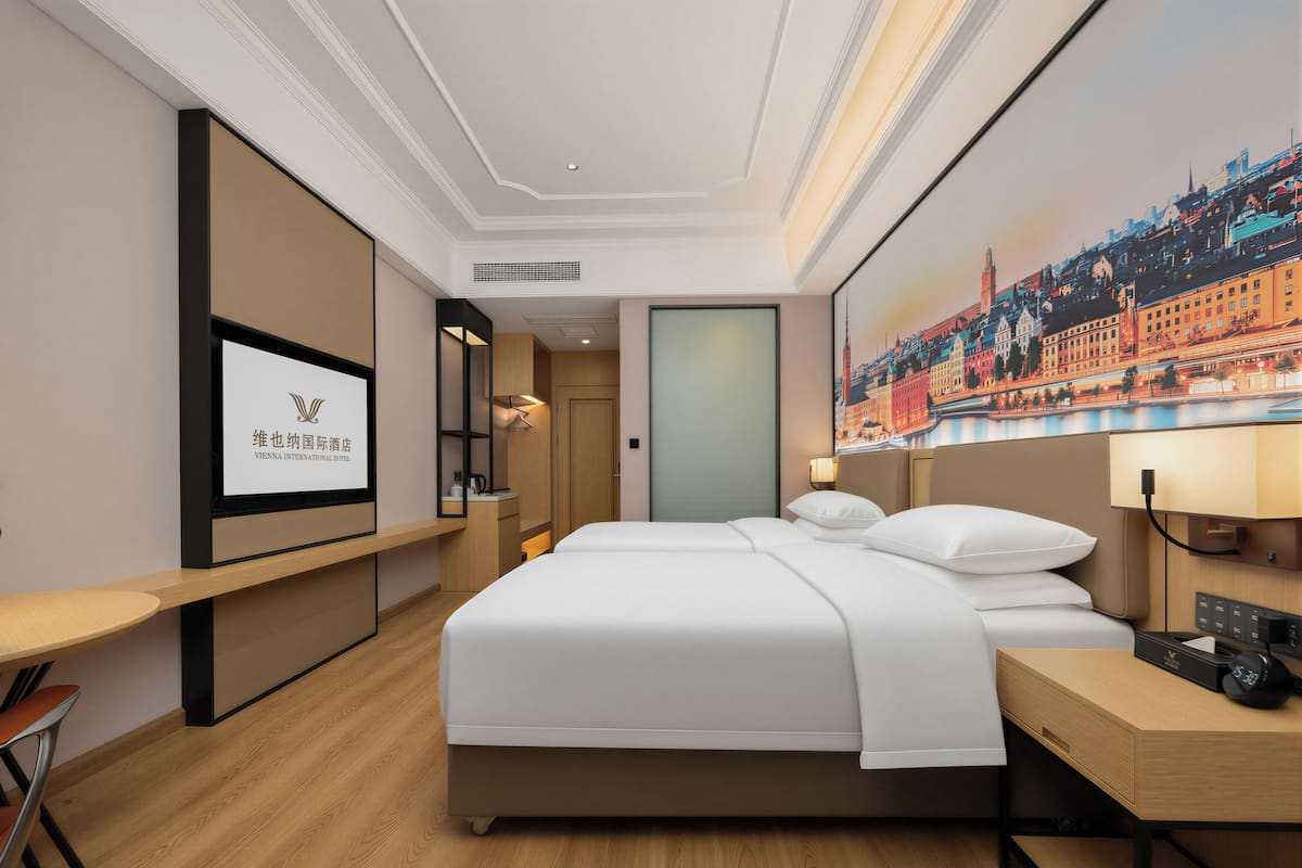 A hotel room with a bed, a desk, a TV, and a painting of a cityscape.