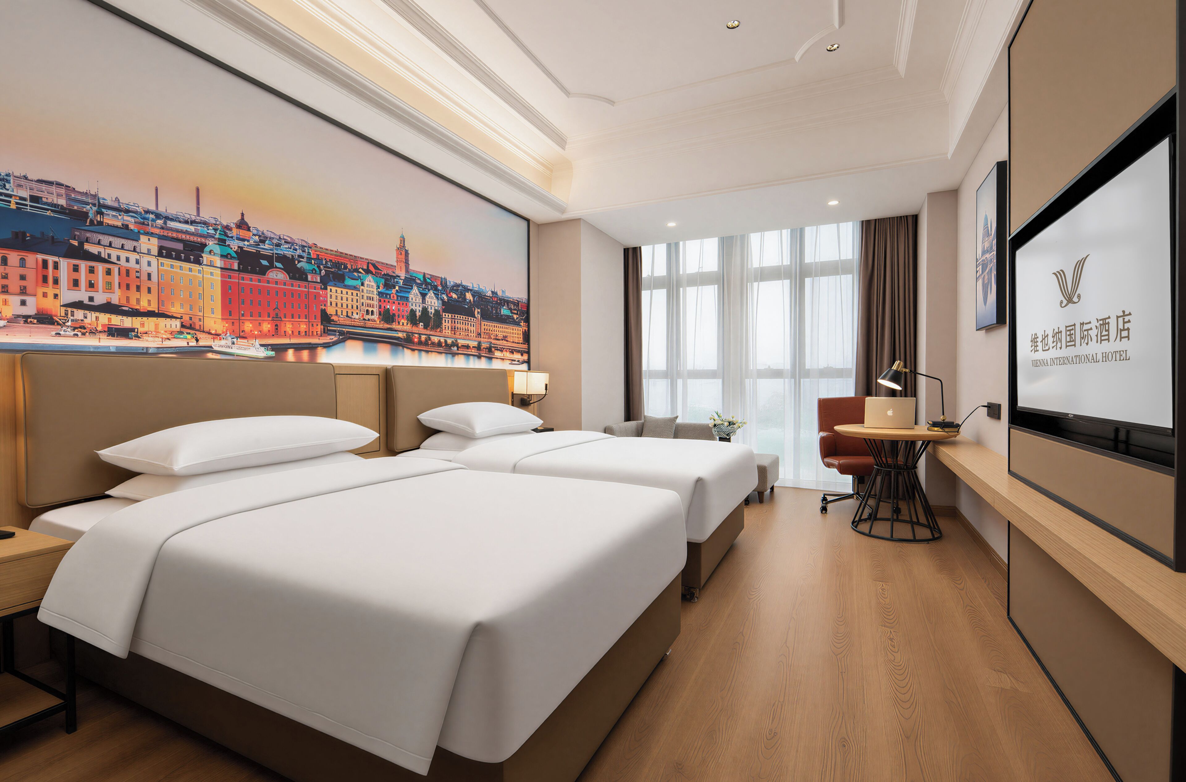 A hotel room with two beds, a desk, a chair, a TV, and a large window.