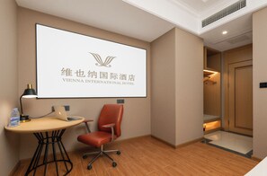 Ein Hotelzimmer mit Schreibtisch, Stuhl und einem großen Bildschirm, der das Logo des Vienna International Hotels zeigt.