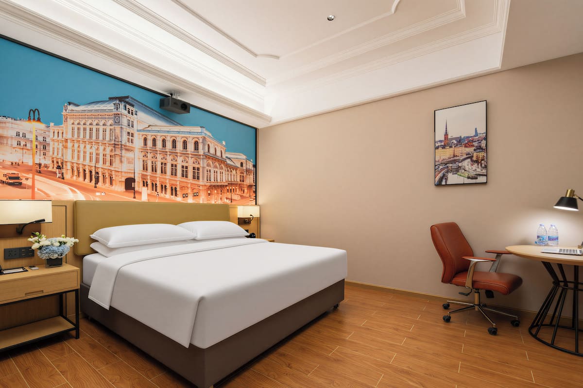 A hotel room with a large bed, a desk with a lamp, a chair, and a desk lamp.