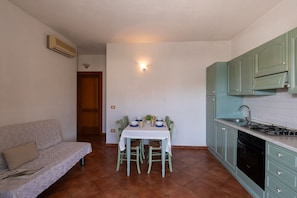 A compact kitchen with green cabinets, a dining table with chairs, and a sofa. - Casa dell'Edera F2/1 by Wonderful Italy (San Teodoro)