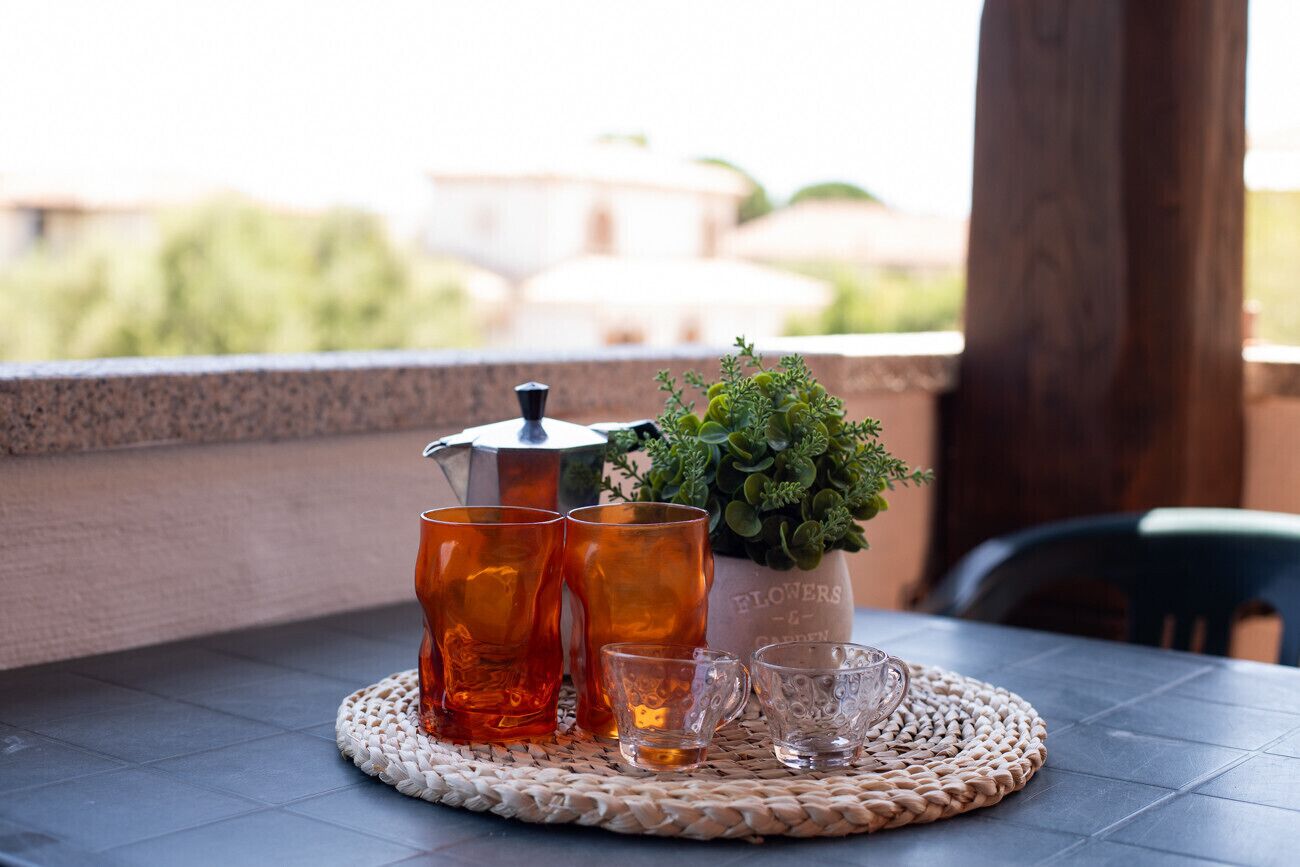 Uma mesa com um sousbento trançado, uma cafeteira e um vaso de planta em uma varanda com vista.