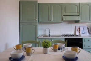 A kitchen with green cabinets, a white tiled backsplash, and a dining table set with bowls and cups. - Casa dell'Edera F2/1 by Wonderful Italy (San Teodoro)