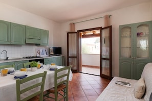 A kitchen with green cabinets, a dining table with chairs, a TV, and a sliding glass door leading to an outdoor area. - Casa dell'Edera F2/1 by Wonderful Italy (San Teodoro)