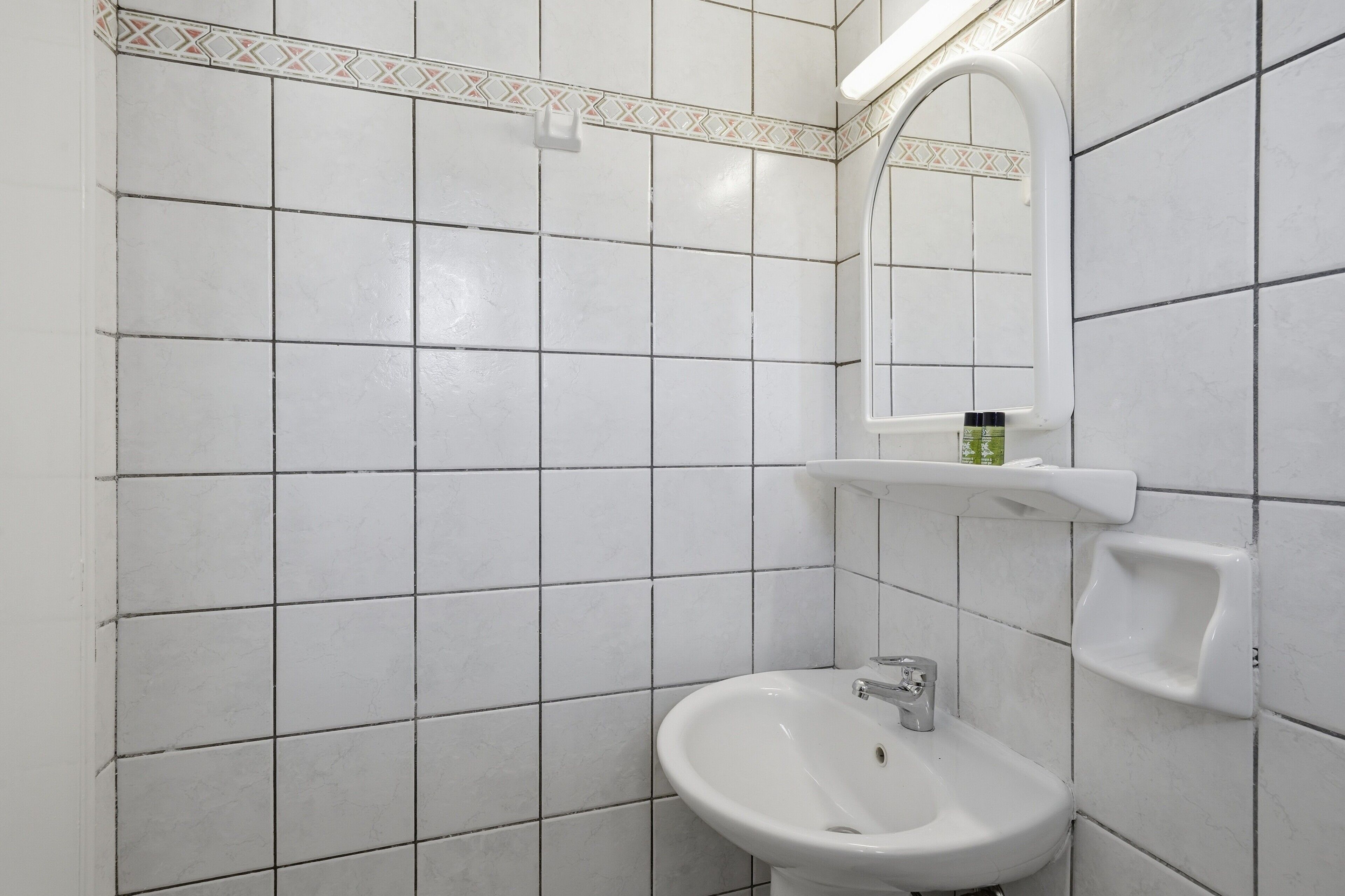 A bathroom with white tiled walls, a white sink, a mirror, and a soap dispenser.