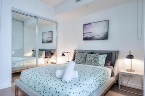 A bedroom with a bed, a bedside table, a lamp, a mirror, and a painting on the wall.