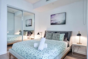 A bedroom with a bed, a bedside table, a lamp, a mirror, and a painting on the wall.