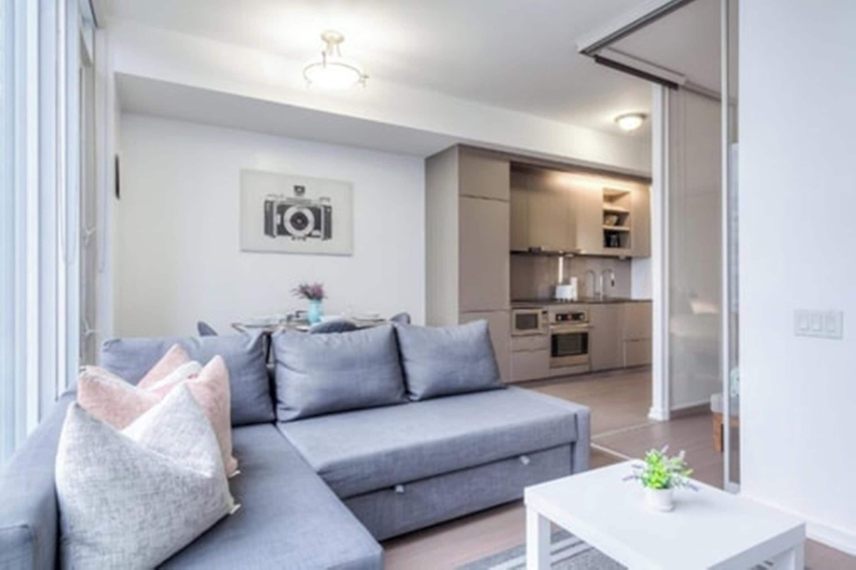 A modern living room with a grey sofa, a small table, and a kitchen in the background.
