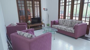 A living room with two purple sofas, a glass coffee table, and a television on a wooden stand. - Green Peak View Haputale (UP)