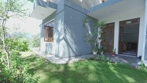A modern two-story house with a well-maintained garden, large windows, and a visible door leading to the interior. - Green Peak View Haputale (UP)