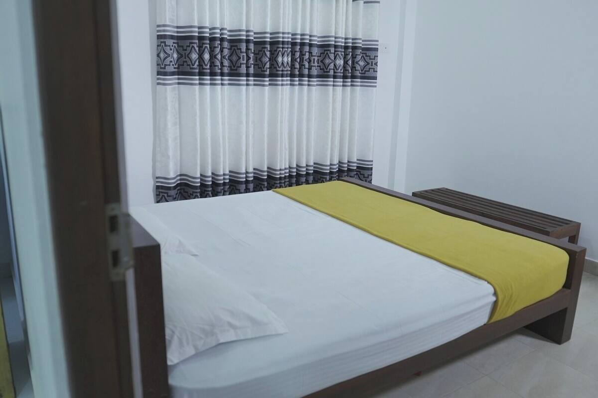 Ein Einzelbett mit gelber Bettdecke, weißen Kissen und einem hölzernen Kopfteil.