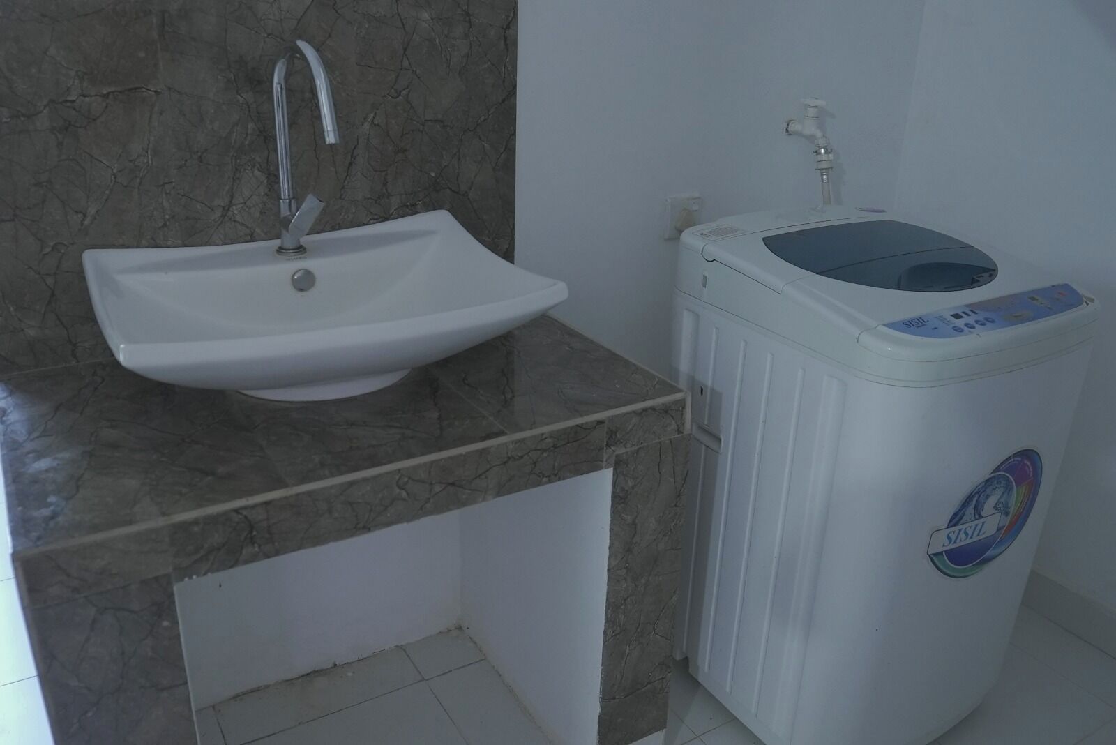 Um banheiro com uma pia branca, bancada de mármore e máquina de lavar branca.