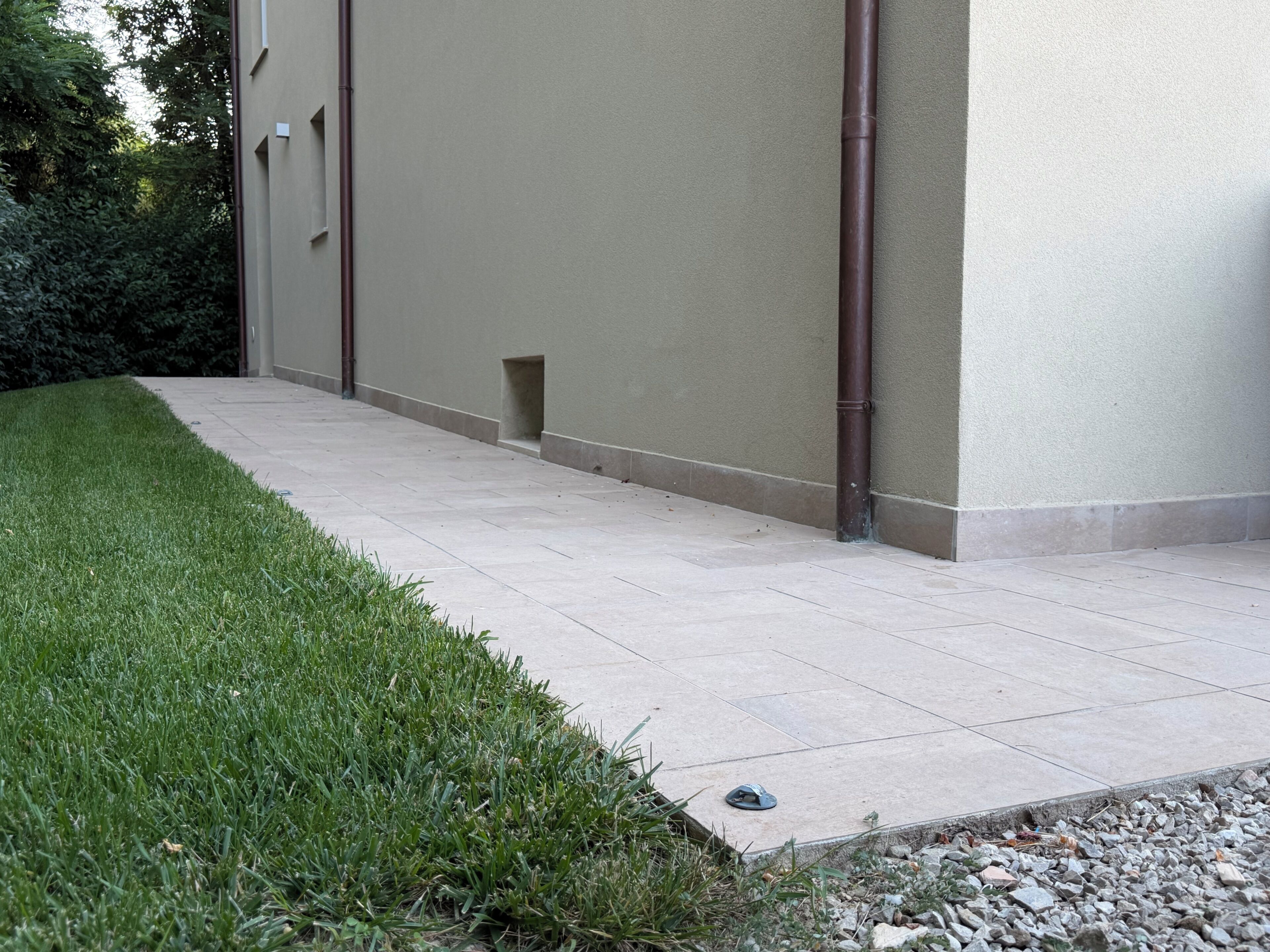 Ein gepflasterter Weg führt zu einem Gebäude mit einer beige farbenen Fassade und einem kleinen Fenster.