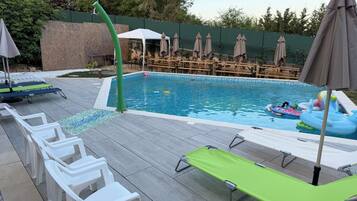 A swimming pool with lounge chairs, a water feature, and a covered seating area.