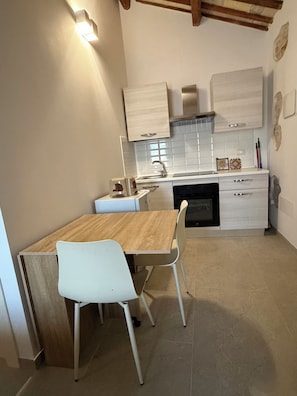 A kitchen with a wooden table and white chairs, a built-in oven, and white cabinets.