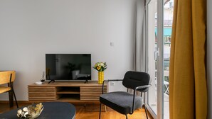 A modern living room with a flat-screen TV, a wooden entertainment unit, a black chair, and a yellow vase with flowers. - Sylka - Warm 1-BR & Balcony in Athens (Athens)