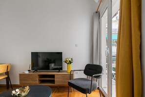 A modern living room with a flat-screen TV, a wooden entertainment unit, a black chair, and a yellow vase with flowers. - Sylka - Warm 1-BR & Balcony in Athens (Athens)