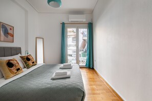 Ein Schlafzimmer mit Bett, Kissen, einem Fenster mit Vorhängen, einem Balkon und einem Deckenventilator.