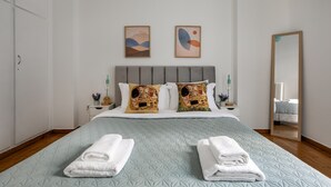 A neatly made bed with a quilted headboard, two pillows with floral patterns, and two towels folded on the bed. - Sylka - Warm 1-BR & Balcony in Athens (Athens)