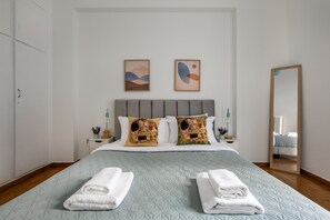 A neatly made bed with a quilted headboard, two pillows with floral patterns, and two towels folded on the bed. - Sylka - Warm 1-BR & Balcony in Athens (Athens)