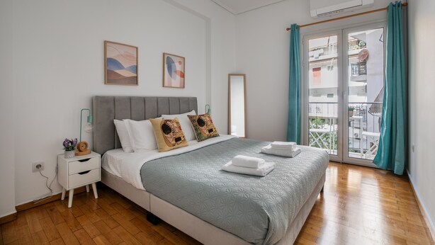 A bedroom with a bed, bedside table, wall art, and a view through a glass door. - Sylka - Warm 1-BR & Balcony in Athens (Athens)