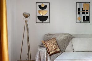 Ein Zimmer mit stehender Stehlampe, einer Couch mit gemusterten Kissen und zwei abstrakten Wandbildern.