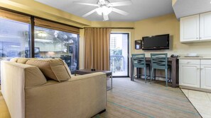 A hotel room with a sofa, dining table, chairs, a TV, and a kitchen area. - Oceanfront 1BR Deluxe at SeaGlass Tower – Myrtle Beach Views & Resort Pools (Myrtle Beach)