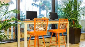 A modern workspace with two laptops, orange chairs, and large windows with a view of palm trees. - Oceanfront 1BR Deluxe at SeaGlass Tower – Myrtle Beach Views & Resort Pools (Myrtle Beach)