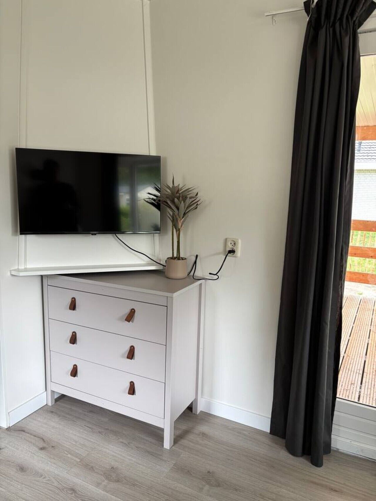 A white cabinet with a flat-screen TV, a potted plant, and a black curtain.