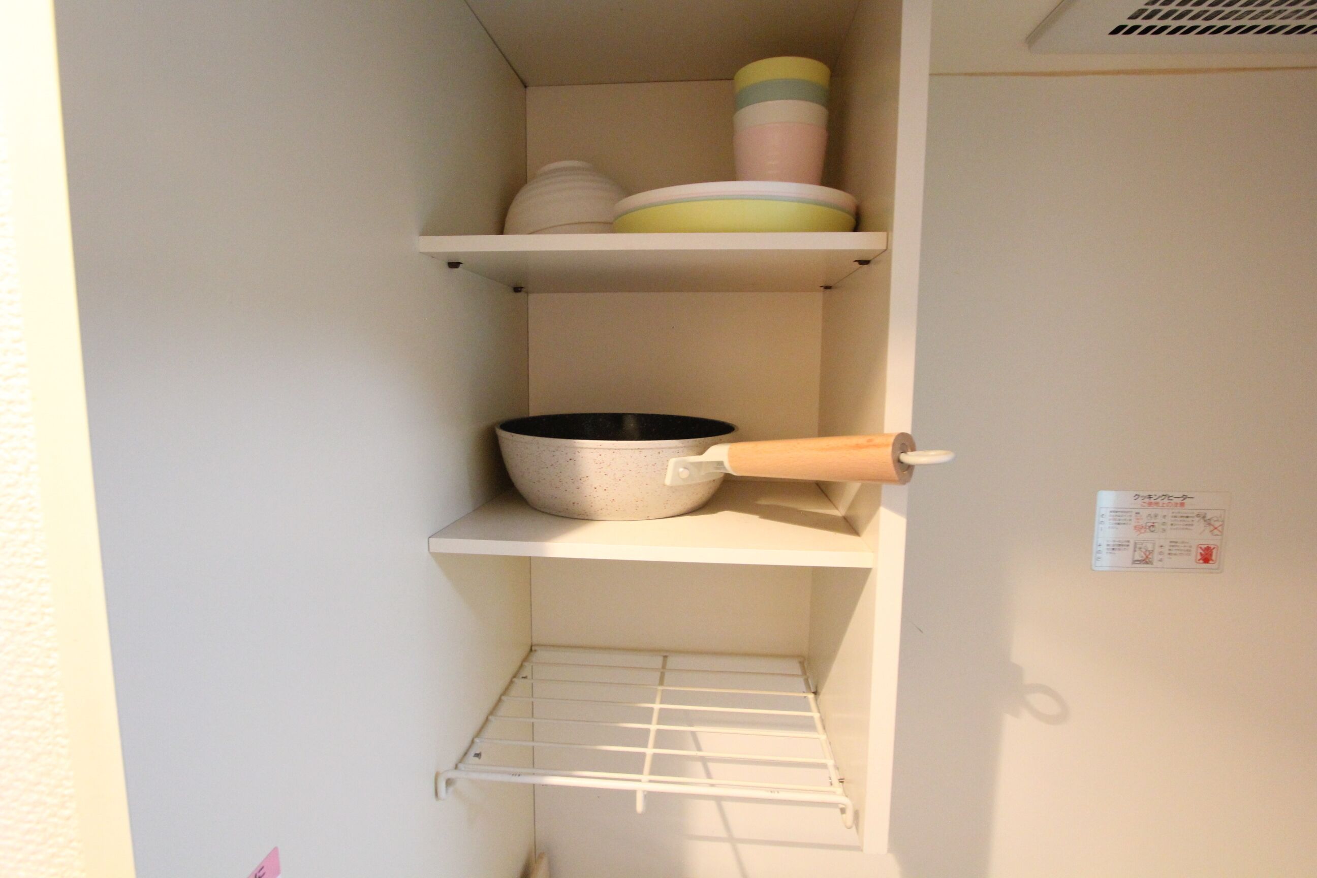 A kitchen with white shelves, a bowl, a rolling pin, and a metal rack.