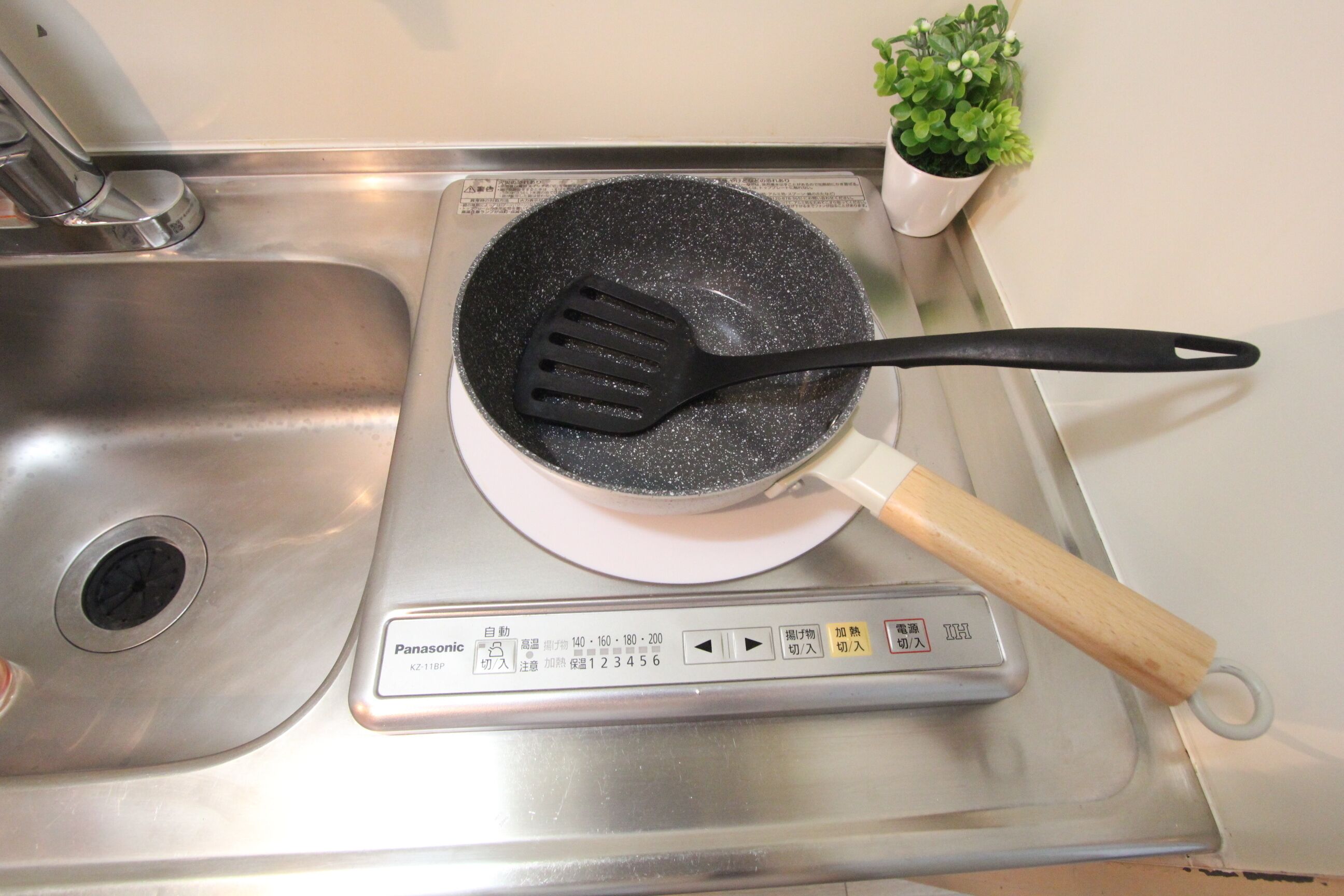 A kitchen with a stove, a black spatula, and a small potted plant.
