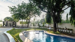 Une piscine bordée de pierres, entourée d’un jardin agrémenté d’arbres et de plantes en pot.