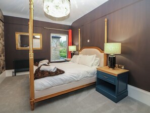 Ein Bett mit Himmelbett, ein Holzkopfteil, ein Nachttisch mit Lampe, ein Spiegel an der Wand und eine Heizung.