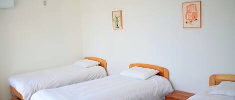 A room with two single beds, a wooden nightstand, a wall-mounted air conditioner, and two framed pictures.