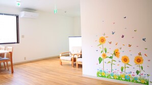 Una habitación con suelo de madera, pared blanca con un mural floral, una silla blanca y una mesa.