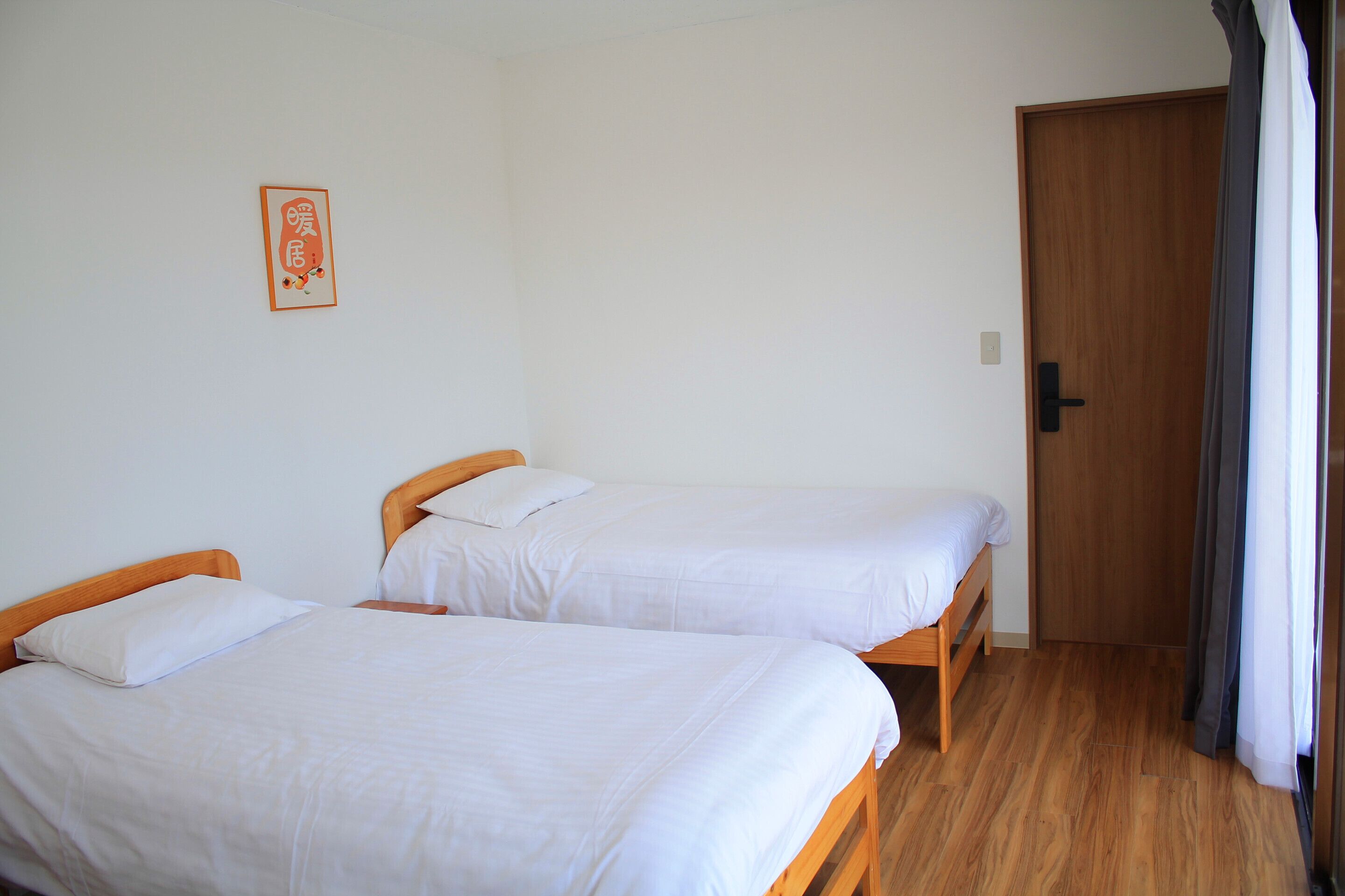 Ein Zimmer mit zwei Holzbett, einer Holztür und einem gerahmten Bild an der Wand.