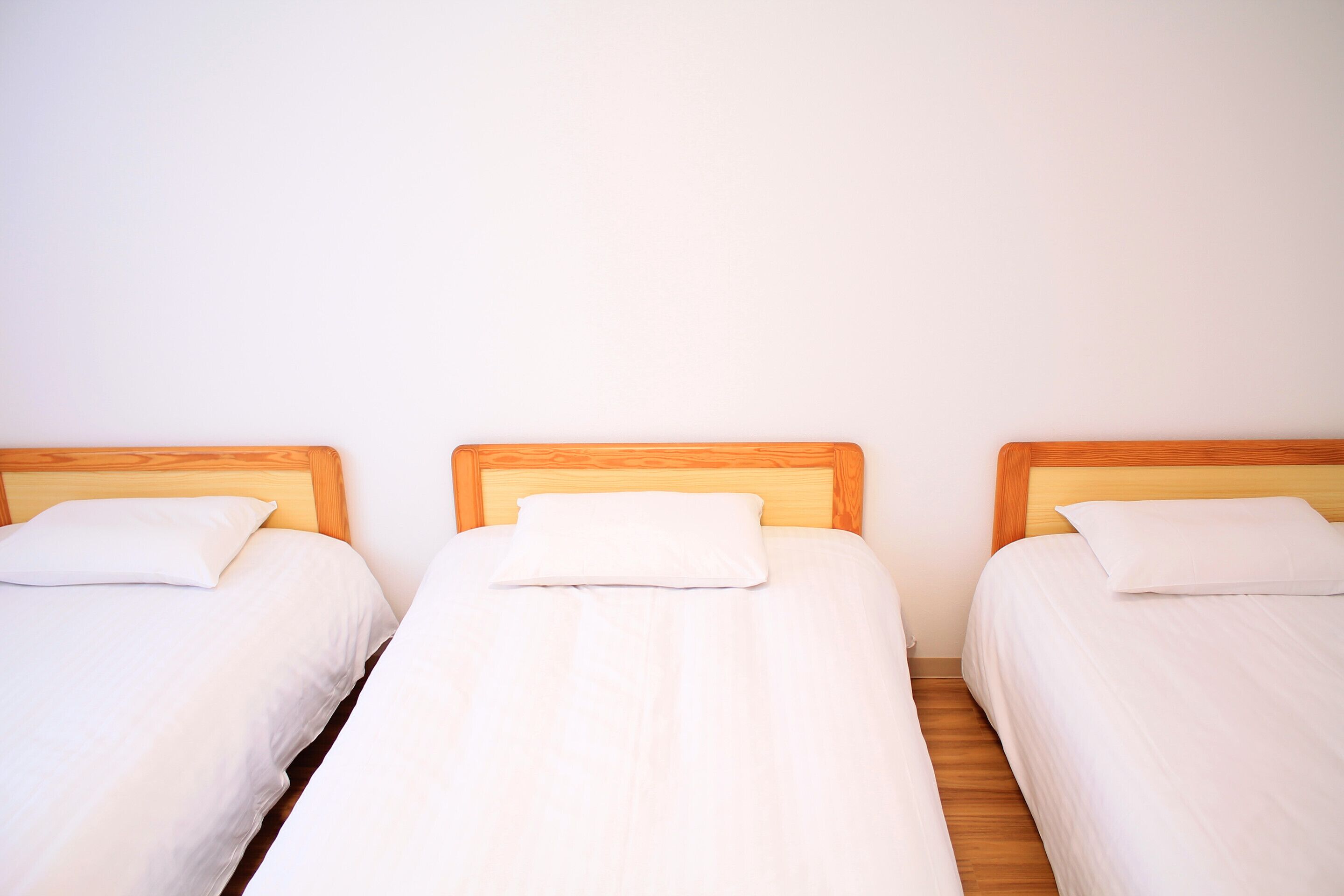 Trois lits simples avec des têtes de lit en bois et du linge de lit blanc, dans une pièce aux murs de couleur unie.