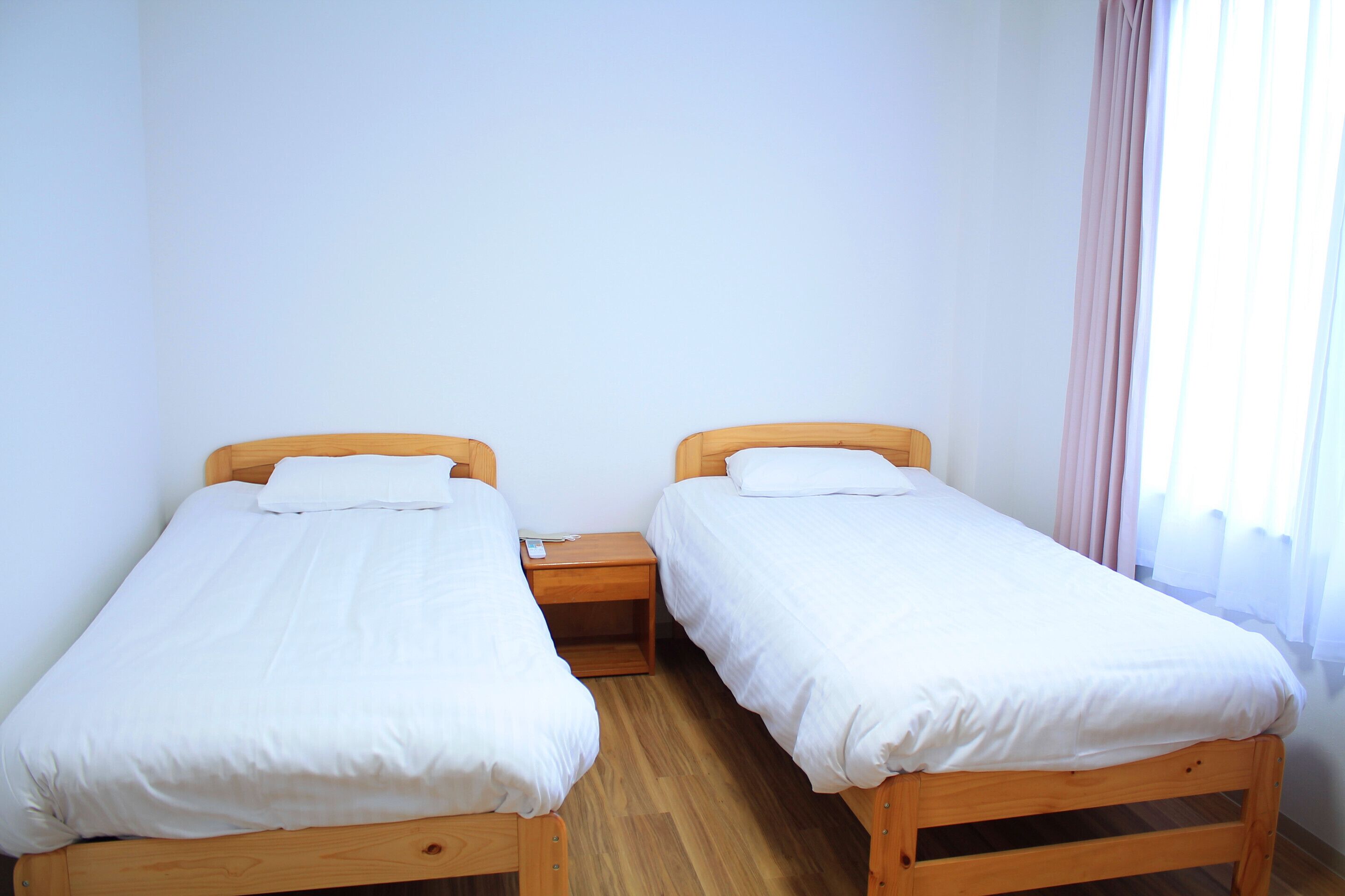 A room with two wooden beds, white bedding, a wooden nightstand, and a window with curtains.
