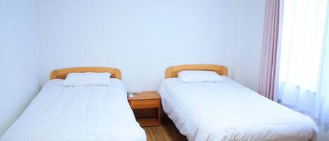 A room with two wooden beds, white bedding, a wooden nightstand, and a window with curtains.