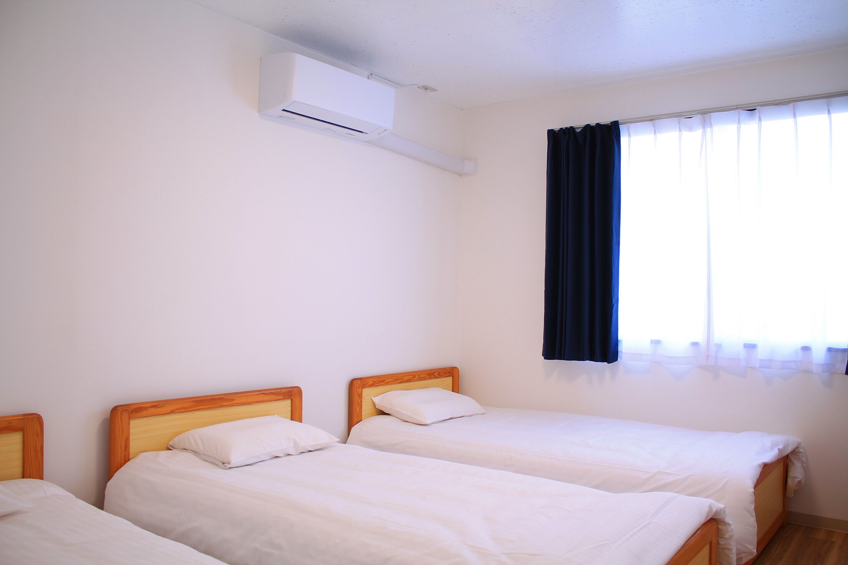 Ein Zimmer mit zwei Einzelbetten, einem Fenster mit Vorhängen und einer Klimaanlage.