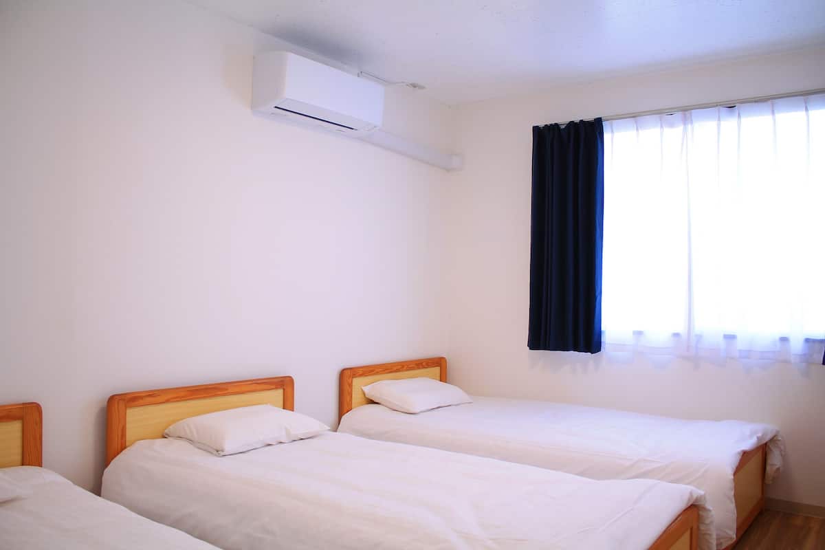 Et værelse med to enkeltsenge, et vindue med gardiner og en aircondition.