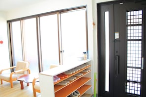 Ein Zimmer mit Schuhablage, einem Sessel und einer Tür mit Gittermuster.