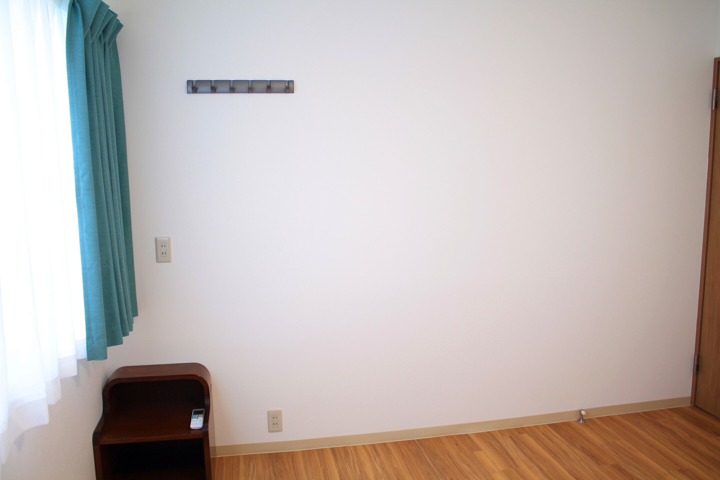 Una habitación con piso de madera, una mesita de madera pequeña, un cortinero azul aguamarina y un enchufe instalado en la pared.