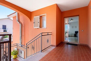 Un balcon doté d’une balustrade en métal, d’un pot de fleurs et offrant une vue sur un immeuble avec un toit recouvert de tuiles.